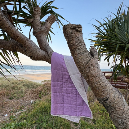 Purple quilt draped over a tree branch with a beach and ocean in the background